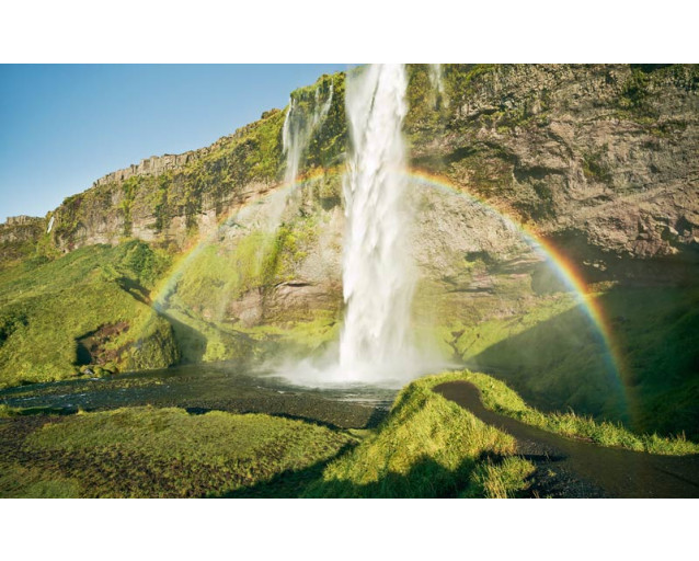 Seljalandsfoss Wasserfall in Island mit einem Regenbogen in der Landschaft.