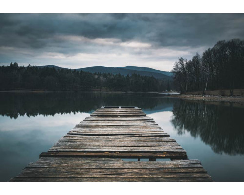 Fototapete mit einem Holzsteg, der sich über einen ruhigen See erstreckt, umgeben von einer üppigen Naturlandschaft.