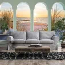 Eine Fototapete mit 3D-Blick auf die Dünen, den Strand und das Meer bei Sonnenuntergang in einem stimmungsvollen Wohnzimmer.