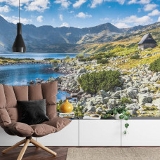 Eine Fototapete mit einem Bergsee und klarem blauen Wasser, umgeben von Bergen in einem Wohnzimmer.