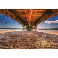 Blick unter einem Pier, der sich über ein ruhiges Meer erstreckt, mit dem Sonnenuntergang in der Ferne, Fototapete für eine ruhige und beruhigende Atmosphäre.