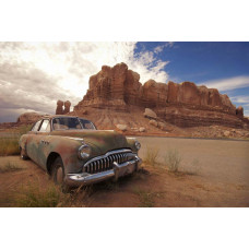 Fototapete eines alten Autos in einer Wüstenlandschaft zwischen Felsen, mit einem klaren blauen Himmel.