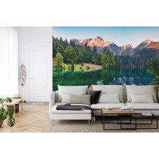 Eine Fototapete mit einem spiegelnden Bergsee, umgeben von Wäldern und Bergen, abgebildet in einem Wohnzimmer.