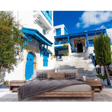 Eine Fototapete mit einer Straße in Tunesien, umgeben von blauen Häusern und traditionellen Details, ideal für ein Schlafzimmer.