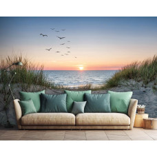 Fototapete mit Strand, Dünen und Meer bei Sonnenuntergang mit Vögeln und warmen Orangetönen, platziert in einem modernen Wohnzimmer.