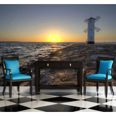 Eine Fototapete von einem Strand mit einem Leuchtturm und einer Windmühle bei Sonnenuntergang, geeignet für ein Büro.