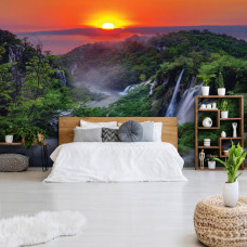 Eine Fototapete mit einem Sonnenuntergang in den Bergen mit Wasserfällen und Natur, zu sehen im Schlafzimmer.