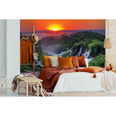 Eine Fototapete mit einem Sonnenuntergang in den Bergen mit Wasserfällen und Natur, zu sehen im Wohnzimmer und Schlafzimmer.