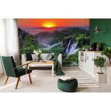 Eine Fototapete mit einem Sonnenuntergang in den Bergen mit Wasserfällen und Natur, zu sehen im Wohnzimmer.