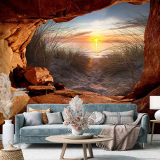 Eine Fototapete von einem Sonnenuntergang aus einer Höhle mit Blick auf die Dünen und das Meer im Vliesbehangstil für ein Wohnzimmer.