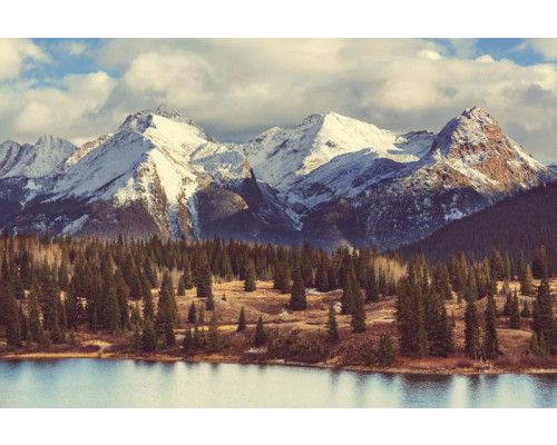 Fototapete mit imposanten Berggipfeln, umgeben von dichten Wäldern und strahlend blauem Himmel.