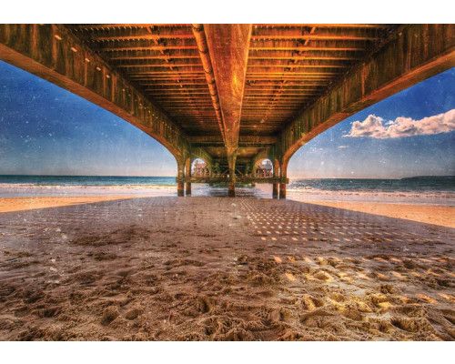 Blick unter einem Pier, der sich über ein ruhiges Meer erstreckt, mit dem Sonnenuntergang in der Ferne, Fototapete für eine heitere und beruhigende Atmosphäre.