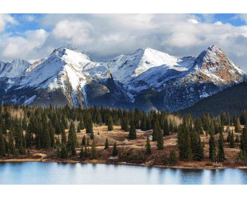 Fototapete mit schneebedeckten Berggipfeln über einem dicht bewaldeten Gebiet, eingefangen in einer wunderschönen Naturlandschaft.