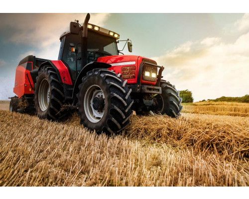 Fototapete Traktor auf dem Feld; ein starker Traktor macht Strohballen auf einem Feld.