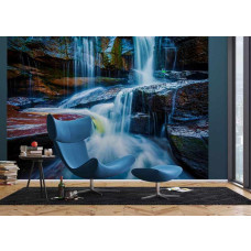 Wohnzimmer mit Fototapete Wasserfall zwischen Felsen, blauem Sessel und passendem Fußhocker.