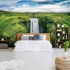 Eine Fototapete mit einem großen Wasserfall in einer Berglandschaft, die im Schlafzimmer zu sehen ist.
