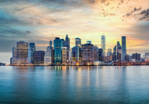Fototapete New York Skyline bei Sonnenuntergang mit Wolkenkratzern und Spiegelung im Wasser.