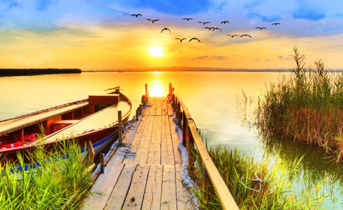 Fototapete eines Sonnenuntergangs über einem Steg mit Blick auf einen See, umgeben von einer friedlichen Naturlandschaft.
