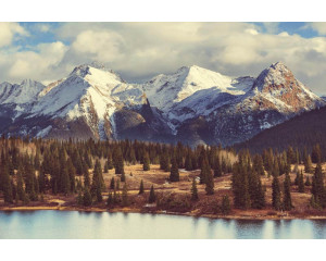 Fototapete mit imposanten Berggipfeln, umgeben von dichten Wäldern und strahlend blauem Himmel.