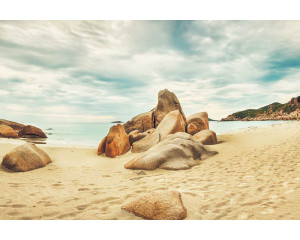 Fototapete von Felsen am Strand, die sich zum Meer hin erstrecken, mit einer ruhigen und friedlichen Landschaft im Hintergrund.