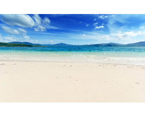 Fototapete mit einem klaren blauen Meer, das an den Strand gespült wird, mit einem klaren blauen Himmel im Hintergrund.